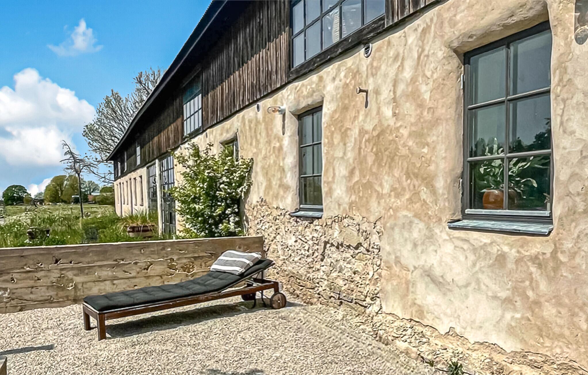 A building with a stone exterior, a wooden deck, and a lounge chair.