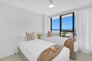 A hotel room with two beds, a large window with a view of the beach, and a ceiling light.