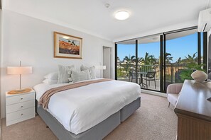 A bedroom with a large bed, a nightstand, a lamp, a framed picture, and a view of the outdoors. -  Oceanfront Escape - SeaHaven on Albatross Avenue (Mermaid Beach)