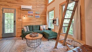A cozy room with a green sectional sofa, a round coffee table, and a ladder leaning against a window.