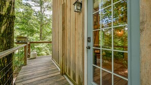 A wooden deck with a glass door leading to a room, surrounded by trees.