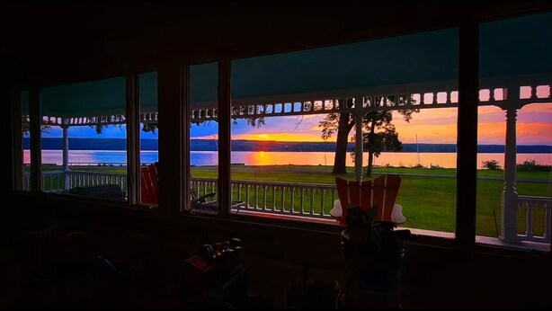 Ein Zimmer mit großen Fenstern, die Blick auf einen Sonnenuntergang über dem Wasser bieten.