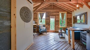 A rustic wooden interior with a high ceiling, a dining table, a blue armchair, and a large window. - Wyldkin Treehouse (Scott County)