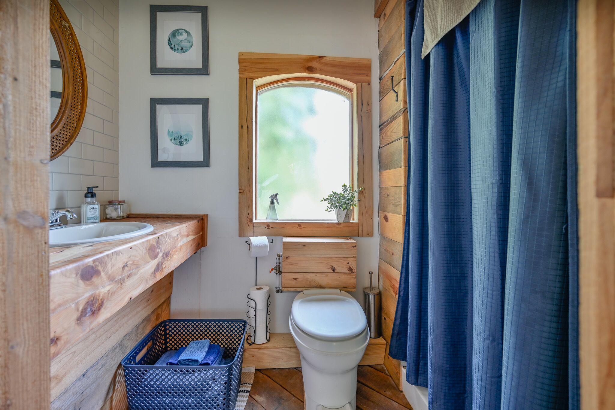 Un baño con tocador de madera, lavamanos, inodoro, ventana y cortina azul.