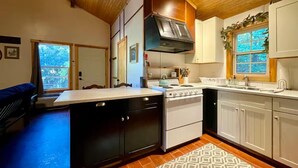 A compact kitchen with a stove, oven, and white cabinets. - Cedar Loft Suite at Sacred Pines Lodge (Scott County)