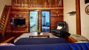 A cozy room with a wooden ceiling, a television, a sofa, a chair, and a bed. - Cedar Loft Suite at Sacred Pines Lodge (Scott County)