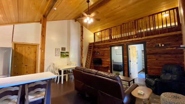 A wooden interior with a dining area, a sofa, and a TV. - Cedar Loft Suite at Sacred Pines Lodge (Scott County)