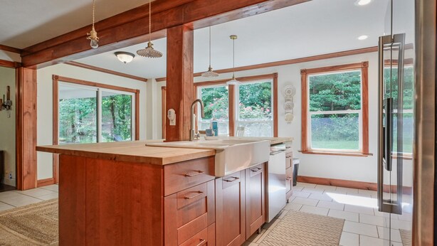 A modern kitchen with wooden cabinetry, a central island, pendant lighting, and large windows offering views of the outdoors. - The Lodge at Sacred Pines (Scott County)
