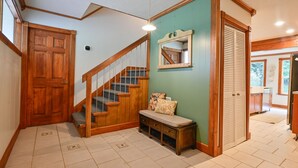 A hallway with a wooden staircase, a bench with cushions, a mirror on the wall, and a door leading to another room. - The Lodge at Sacred Pines (Scott County)