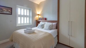 A bedroom with a bed, a nightstand with books, a window, and a wardrobe. - Two bedroom Apartment  (Malahide)