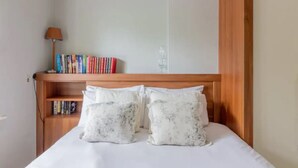A neatly made bed with white linens and floral-patterned pillows, a wooden headboard, a bedside table with a lamp, and a shelf with books. - Two bedroom Apartment  (Malahide)