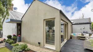 A modern house with a large sliding glass door, a patio with outdoor furniture, and a well-maintained garden. - Two bedroom Apartment  (Malahide)