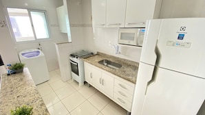 Een moderne keuken met witte kasten, een granieten aanrechtblad, een inbouwoven, een magnetron en een koelkast.