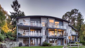 A modern multi-story house with balconies, a well-maintained lawn, and a wooden fence.