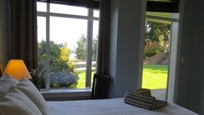 A hotel room with a bed, a lamp, a chair, and a view of a lawn and trees through large windows.