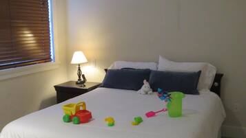 A bedroom with a bed, pillows, a nightstand, a lamp, and toys on the bed.