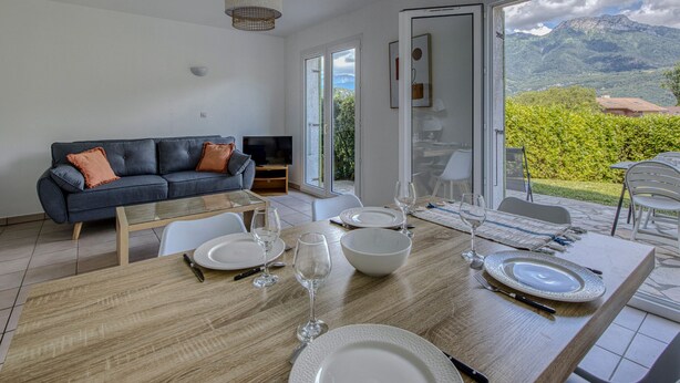 Un salón moderno con un sofá, televisión y comedor con una mesa dispuesta para dos.