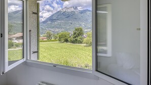 Habitación con un amplio ventanal que ofrece vistas a una montaña y un campo verde.