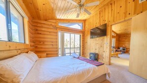 Camera da letto in stile baita con un letto, una ventola a soffitto, una TV e un camino.