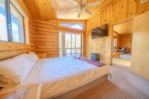 Une chambre située dans un chalet en rondins, avec un lit, un ventilateur de plafond, une télévision et une cheminée.
