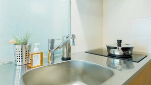 A modern kitchen with a stainless steel sink, a faucet, a potted plant, a soap dispenser, and a pot on the countertop. - Kago  by Tokyo Shukuba Hotel (Tokyo)