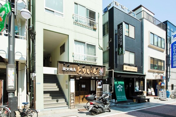 Egy épület, amelyen egy „GUST HOUSE” feliratú tábla és egy másik, „Shinagawa Hotel” feliratú tábla látható. Az épület előtt egy motorkerékpár parkol.