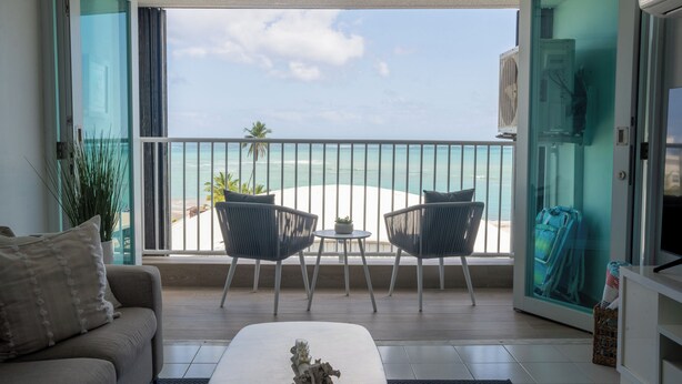 Un balcon avec vue sur la plage, un canapé, deux fauteuils et une petite table agrémentée d’un objet décoratif.
