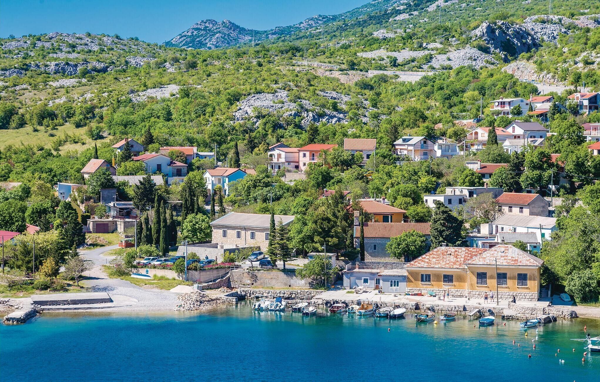 Un villaggio costiero con case, un porto turistico e montagne sullo sfondo.
