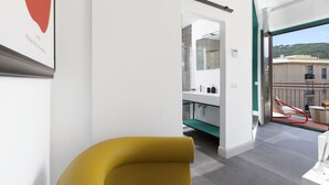 Un interior moderno con una silla amarilla, una pared blanca con una obra de arte enmarcada y un balcón con barandilla roja.