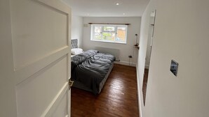 Un pasillo estrecho que conduce a un dormitorio con una cama, una ventana y un radiador.