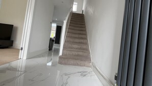 Un pasillo con suelo de mármol, una escalera alfombrada y un radiador negro.
