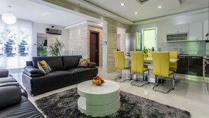 A modern living room with a black leather sofa, a round coffee table with fruit, and a dining area with yellow chairs.