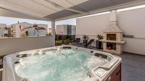A rooftop terrace with a hot tub, lounge chairs, and a stone fireplace.