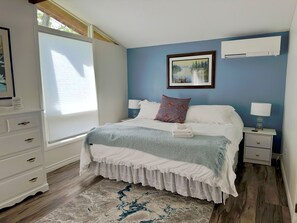 A bedroom with a bed, nightstands, a dresser, a window with blinds, a painting on the wall, and a floor lamp.