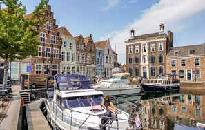 Um canal com barcos atracados, uma mulher em um barco e edifícios históricos ao longo da água.