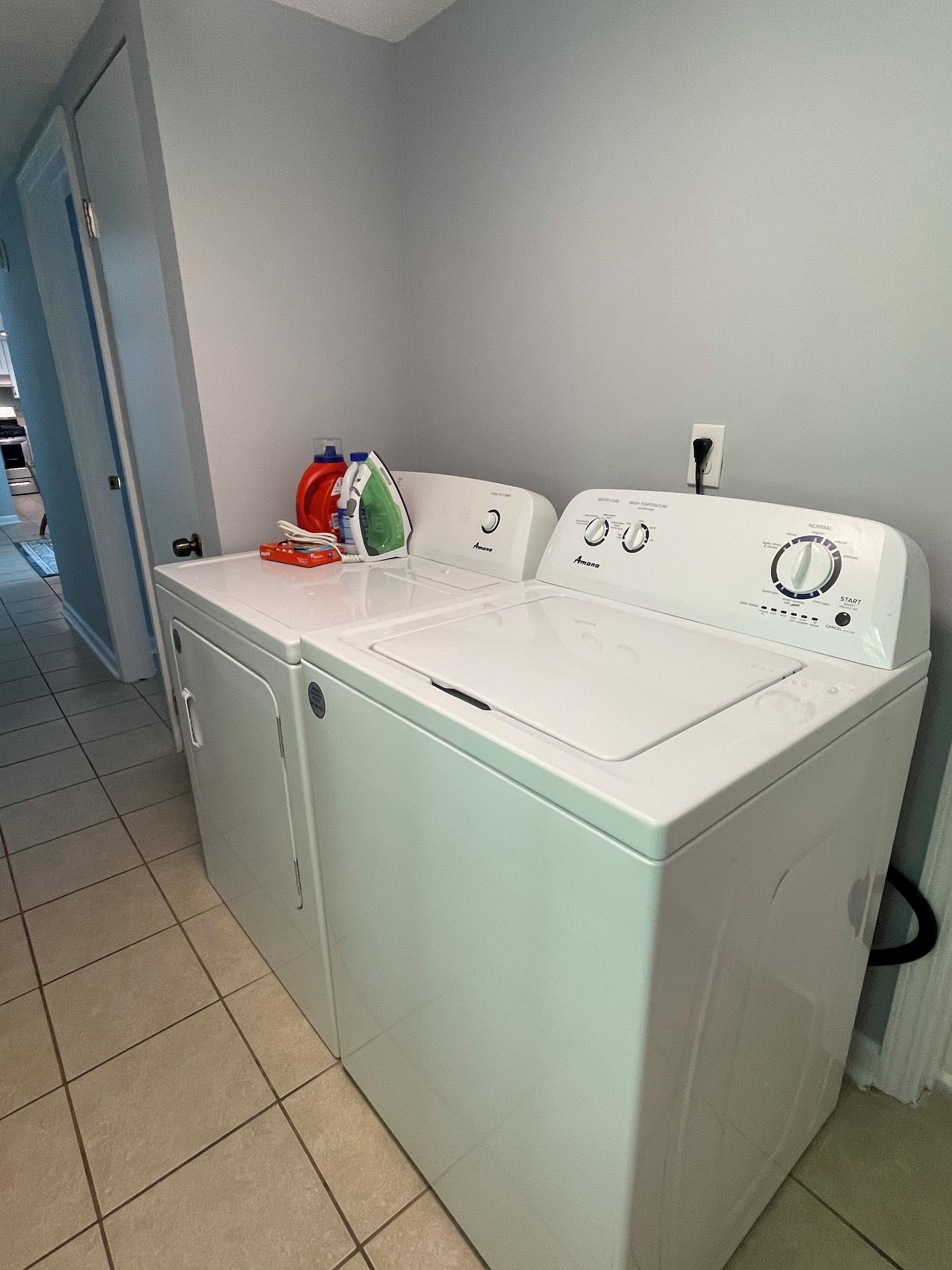 Una lavadora compacta de carga frontal, blanca, con panel de control, un tendedero y un planchado rojo y verde encima.