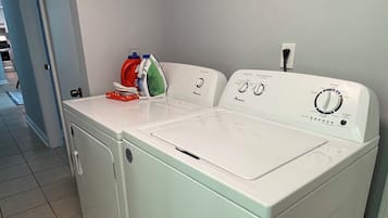 Una lavadora compacta de carga frontal, blanca, con panel de control, un tendedero y un planchado rojo y verde encima.