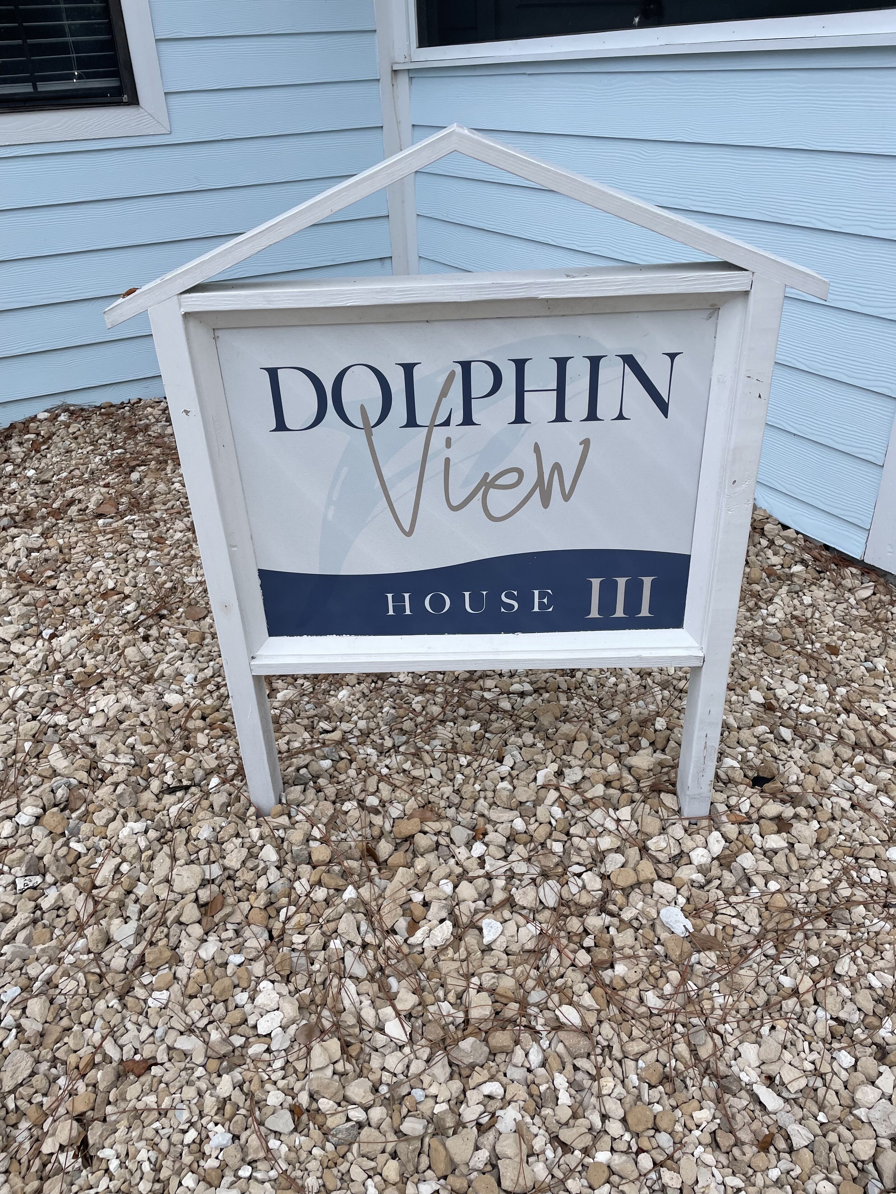 A sign for 'Dolphin View House III' with a simple house-shaped design and a dark blue base.
