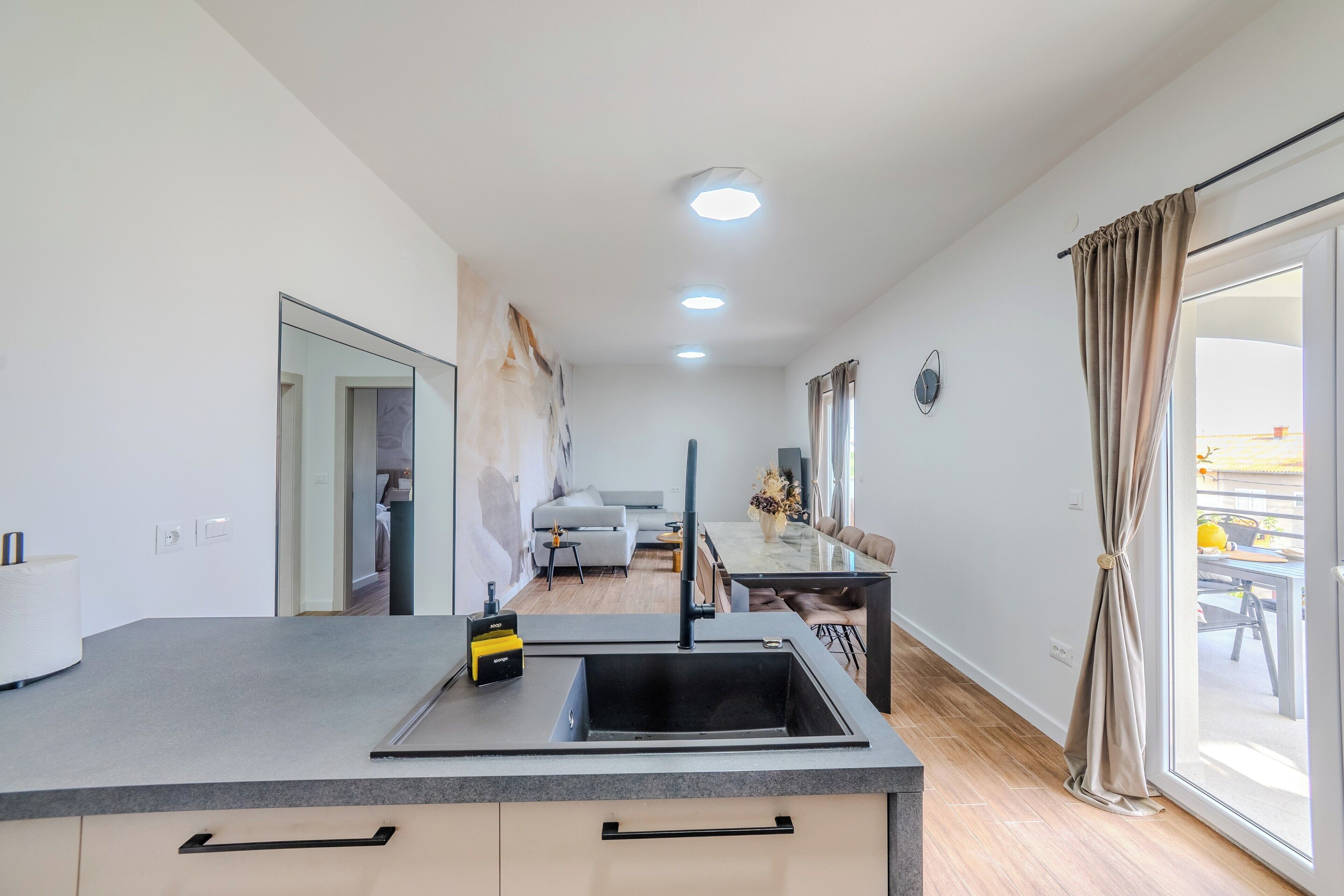 A modern kitchen with a built-in dishwasher, a dining area with a glass table, and a view through a large window.