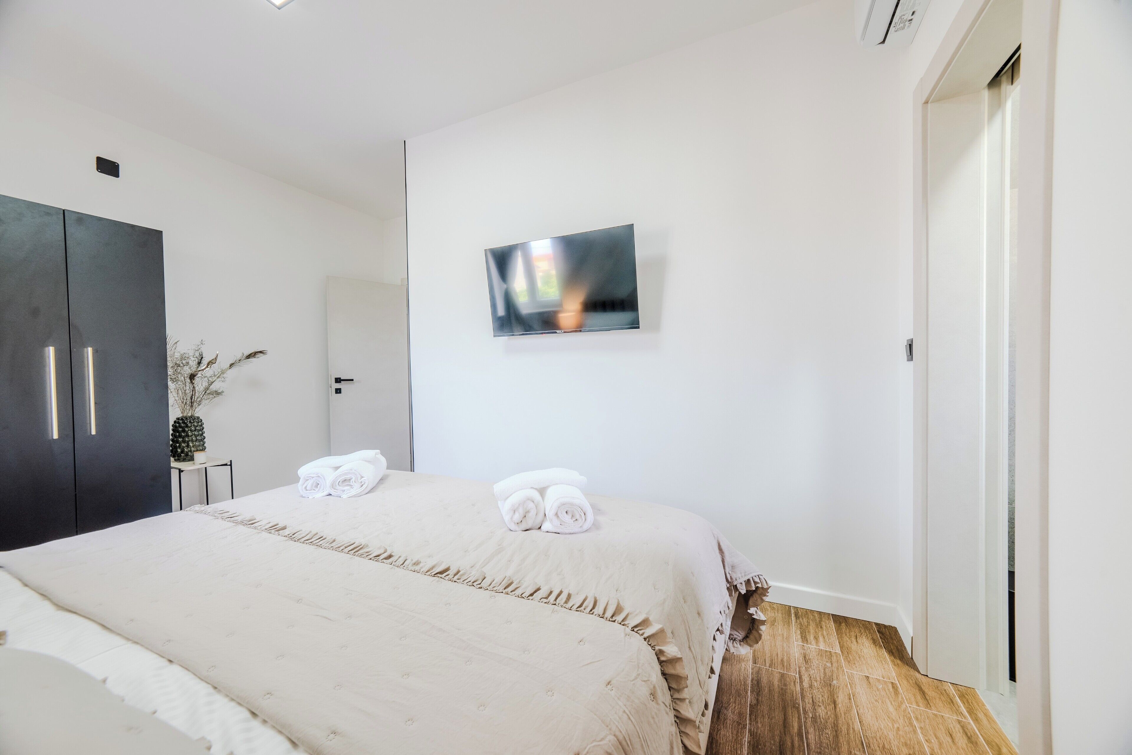 Habitación de hotel con cama, armario, televisor de pantalla plana montado en la pared y una puerta que da a otra habitación.