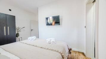 Habitación de hotel con cama, armario, televisor de pantalla plana montado en la pared y una puerta que da a otra habitación.