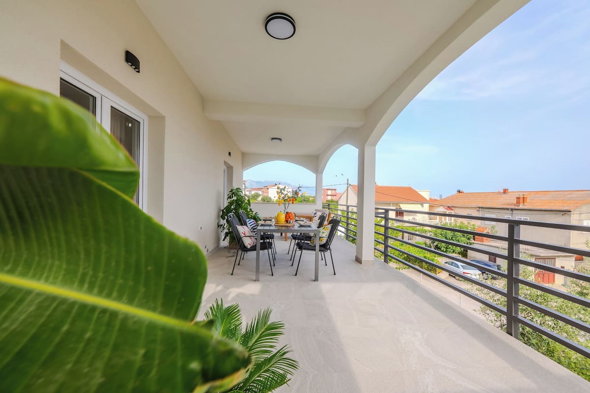 A balcony with a table and chairs, overlooking a residential area with houses and a clear sky.