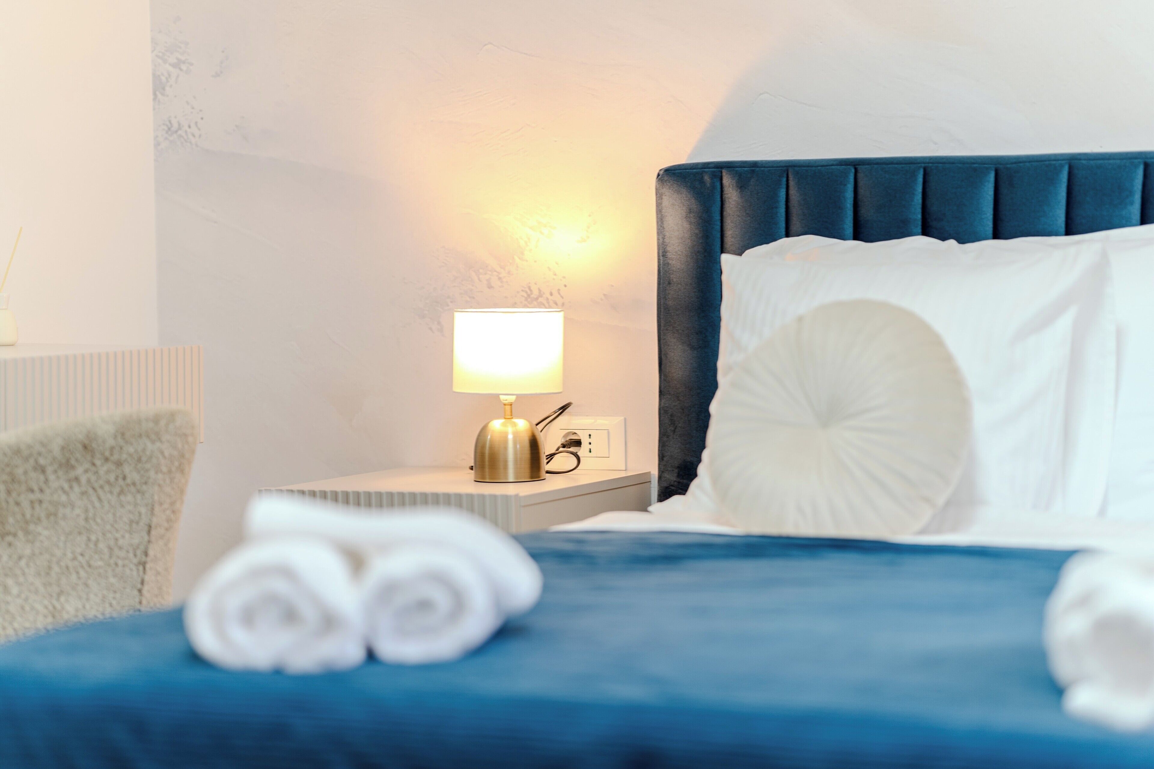 Un lit bien fait, avec une tête de lit bleue, des oreillers blancs et des serviettes enroulées.