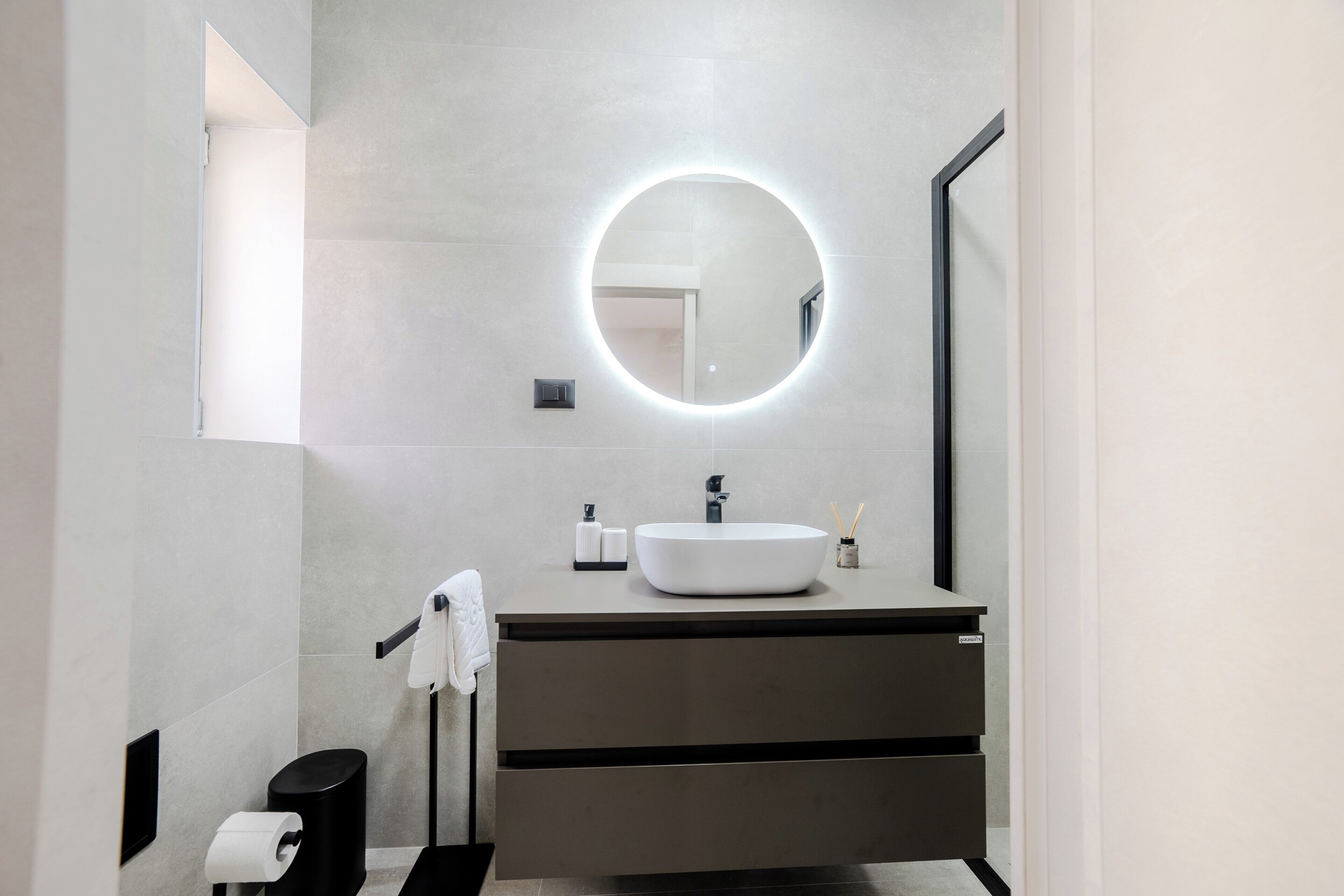 Un baño moderno con un espejo redondo, un lavabo blanco y un perchero para toallas.