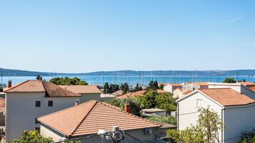 A coastal town with terracotta-roofed buildings, a marina with sailboats, and a clear blue sky.