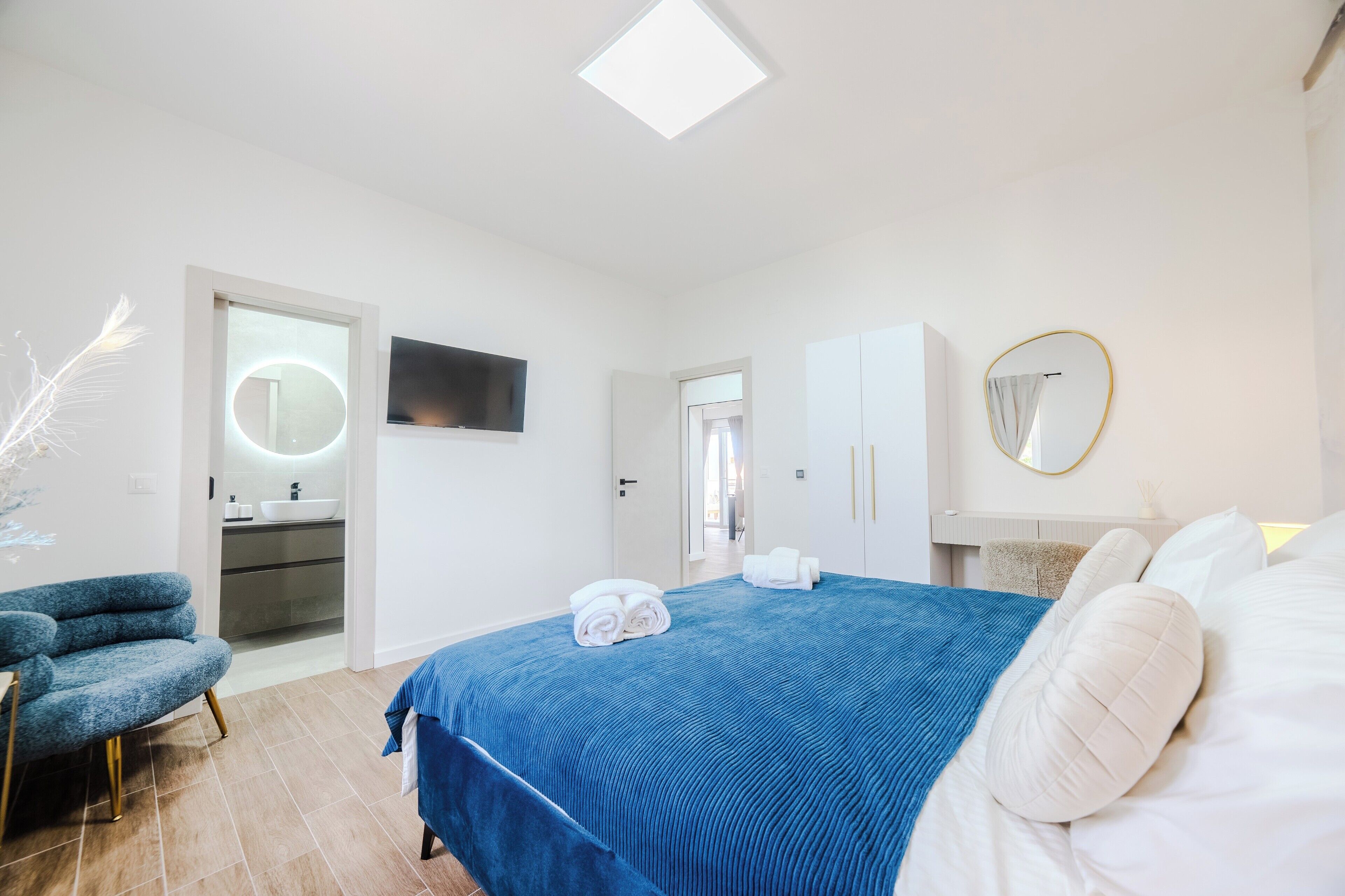 Un dormitorio moderno con una cama grande, un televisor, un baño con lavamanos y una silla.