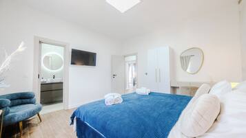 Un dormitorio moderno con una cama grande, un televisor, un baño con lavamanos y una silla.
