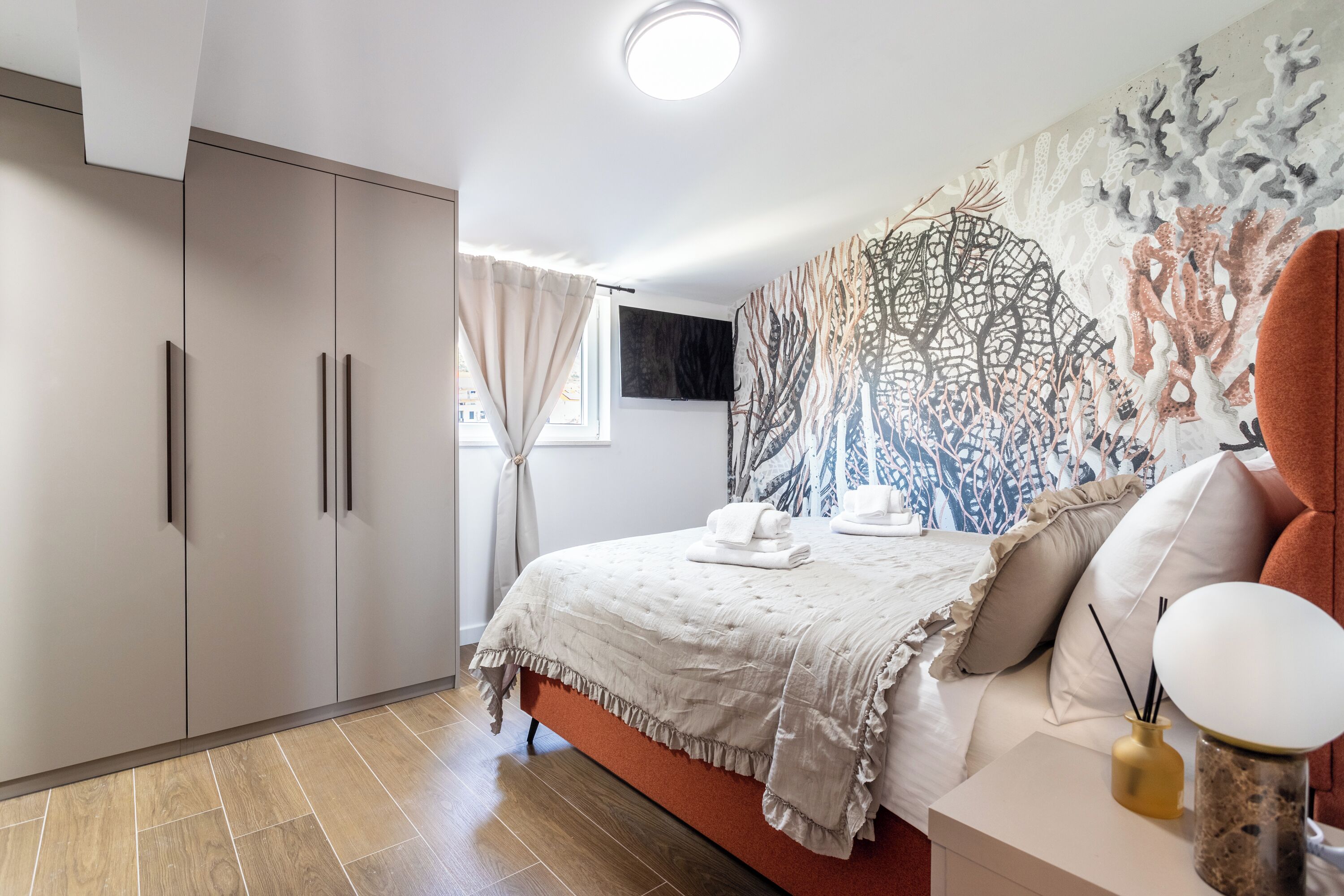 A modern bedroom with a bed, a wardrobe, a tapestry, and a bedside table with a lamp.