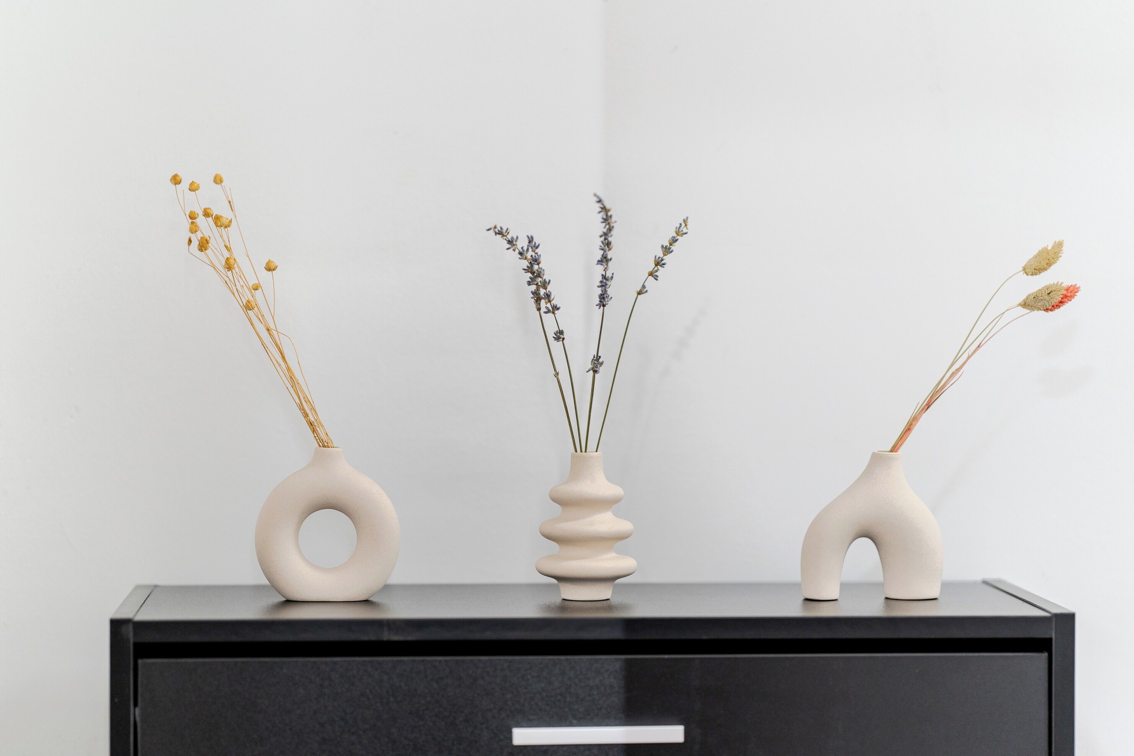 Three vases with dried plants on a black cabinet.