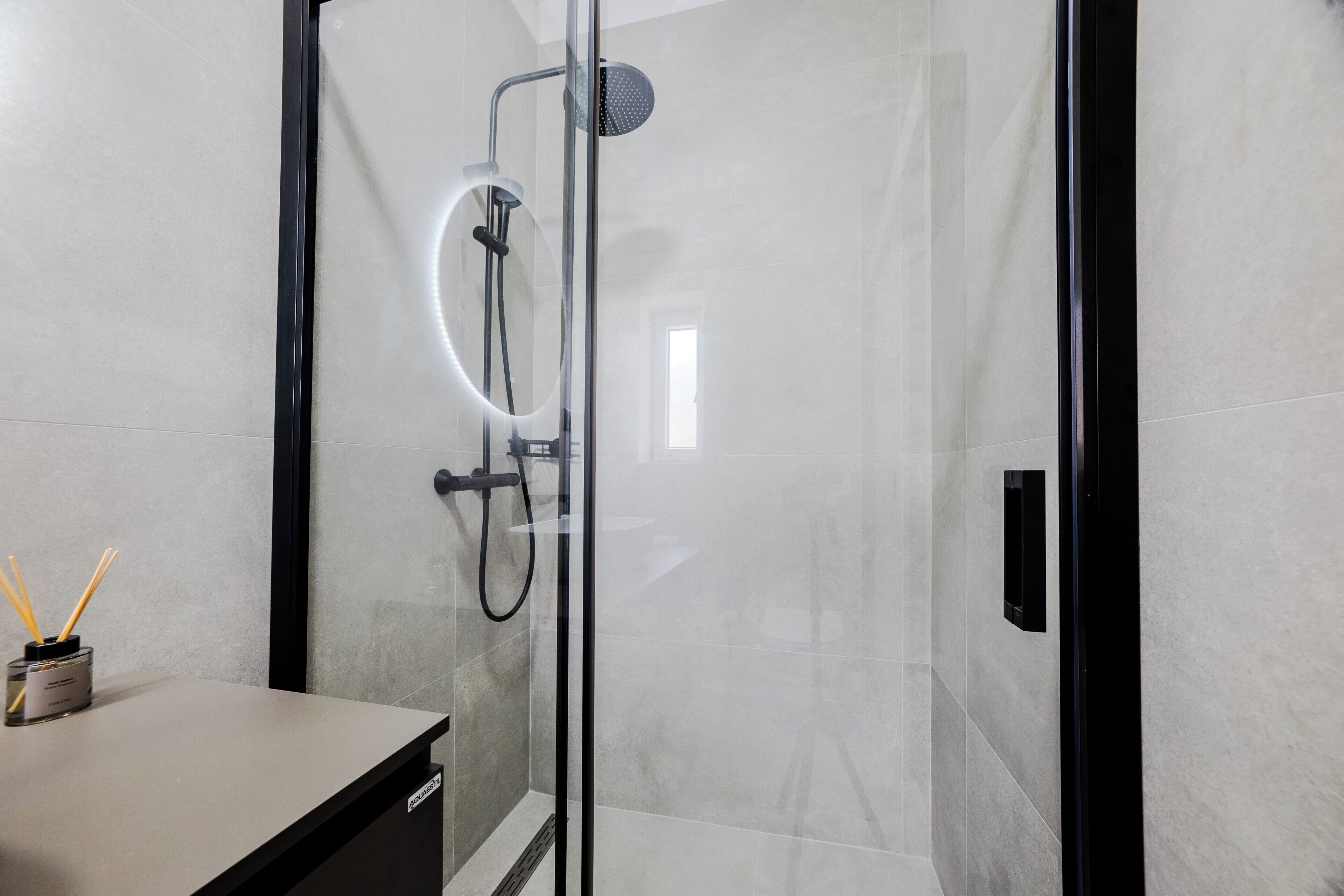 A modern shower with a glass door, a handheld showerhead, and a wall-mounted control panel.